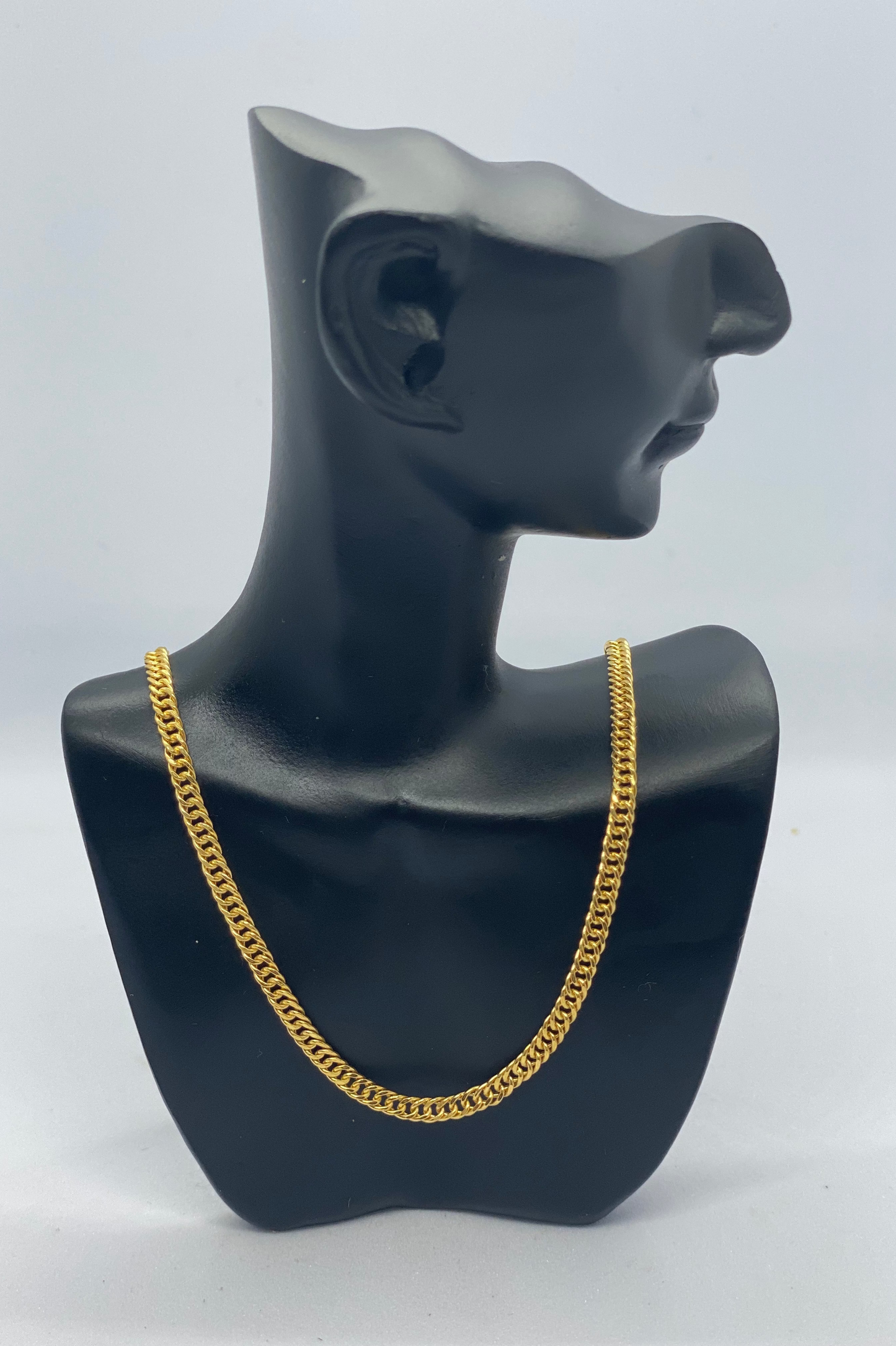 Gold chain necklace on a black mannequin bust against a white background