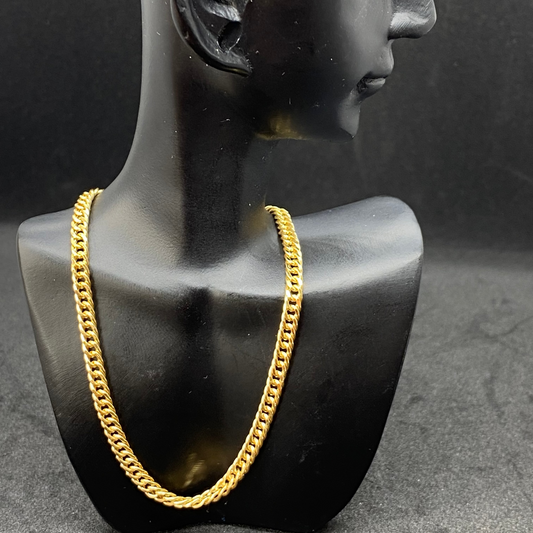 Gold chain necklace on a black mannequin bust against a dark background